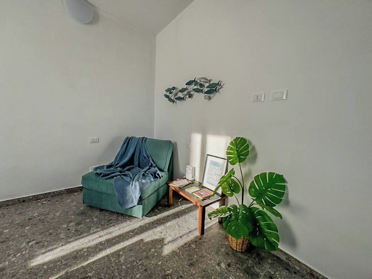 A room with a green sofa, a small table with a plant, and a wall-mounted decorative piece.