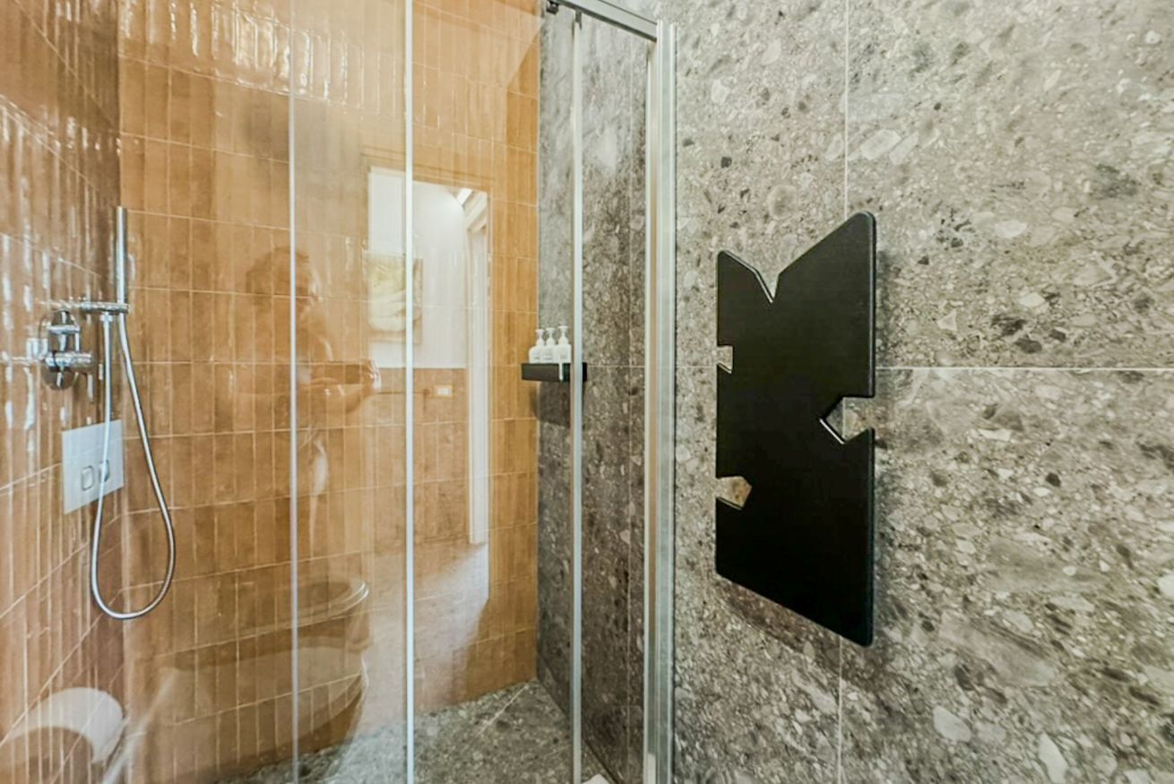 Un angolo doccia con porta in vetro, parete in marmo e cartello nero.