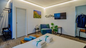 Una habitación de hotel con cama, una silla, una mesita, una planta y obras de arte en las paredes.