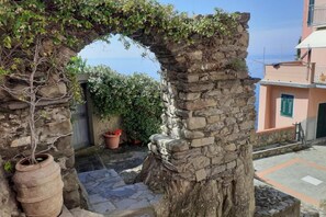 A stone archway, a tree with climbing plants, and a building with a pink facade.
