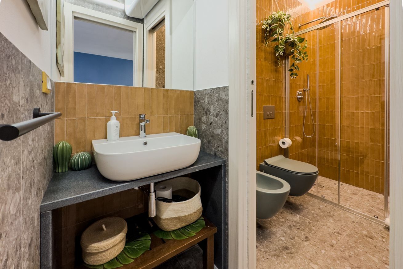 Un baño con lavamanos blanco, espejo, ducha e inodoro.
