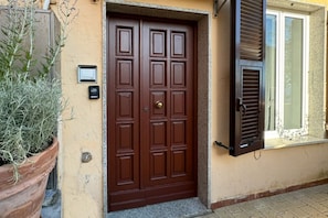 A brown double door with a keyhole, a small potted plant, and a window with shutters.