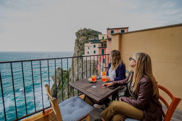 Two people seated at a table with drinks, overlooking a coastal view with buildings.