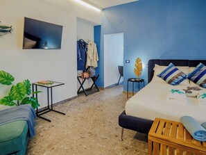A hotel room with a bed, a small table, a chair, a plant, and a coat rack. - Il Sogno di Beatrice Luxury Apartment (Manarola)