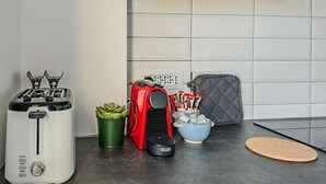 Una cocina con un tostador, un electrodoméstico rojo, una planta verde, un cuenco de aperitivos y un tapete de corcho.