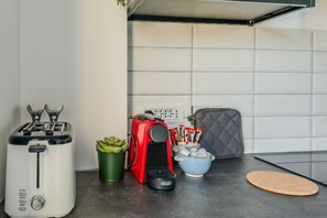 A kitchen with a toaster, a red appliance, a green plant, a bowl of snacks, and a cork mat.