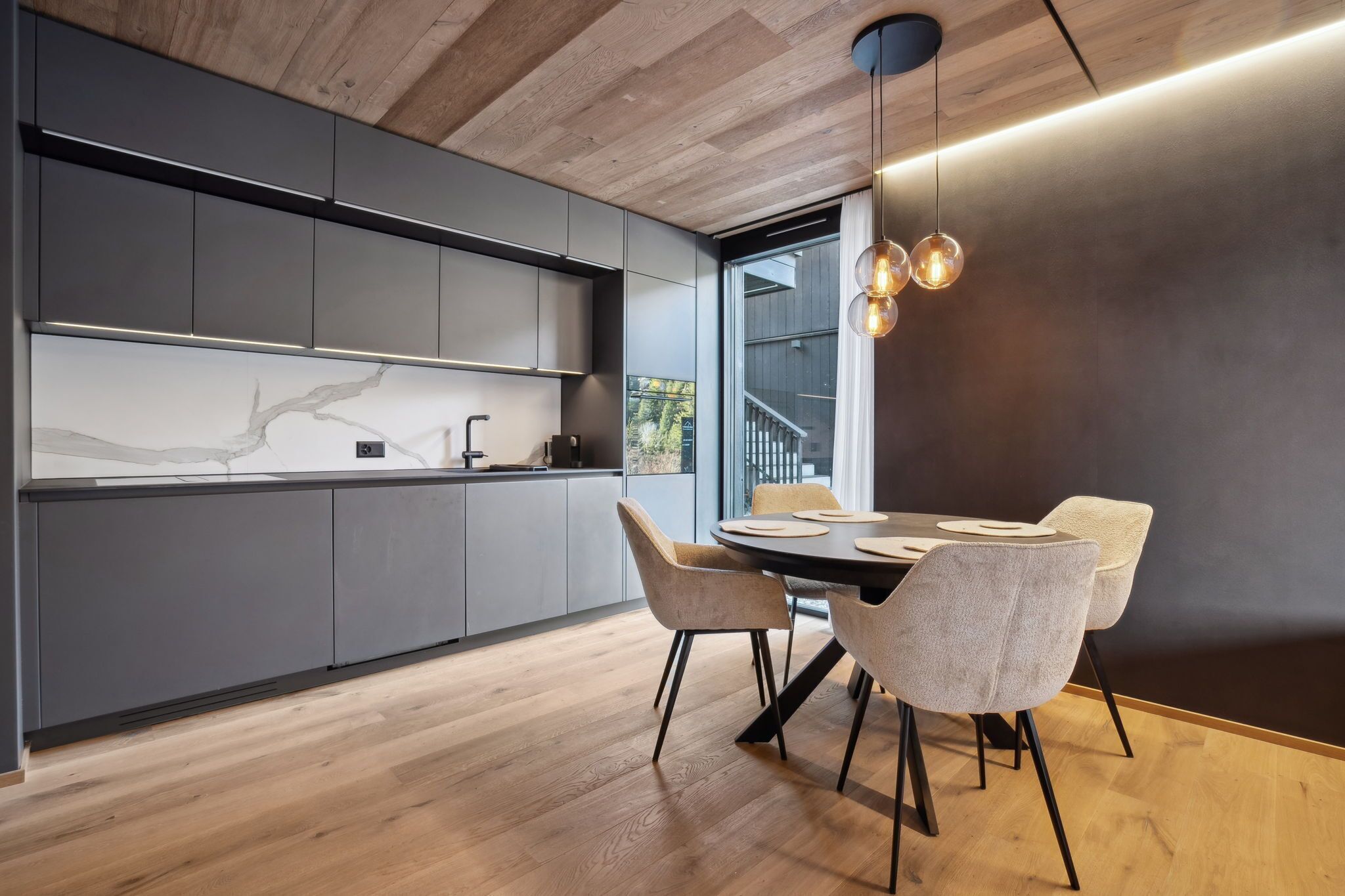 A modern kitchen with grey cabinets, a marble backsplash, and a dining area with a round table and chairs.