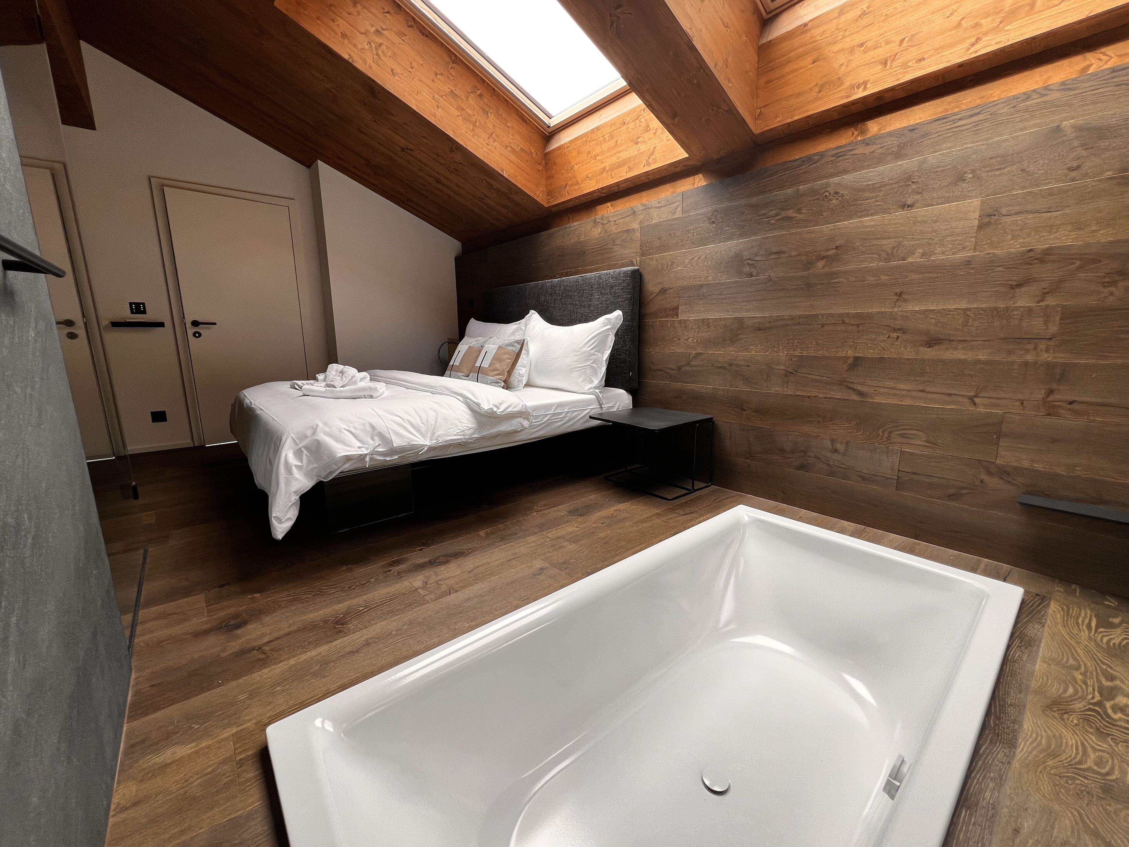 Una camera da letto con un lucernario, pareti in legno, un letto, un comodino e una vasca da bagno.