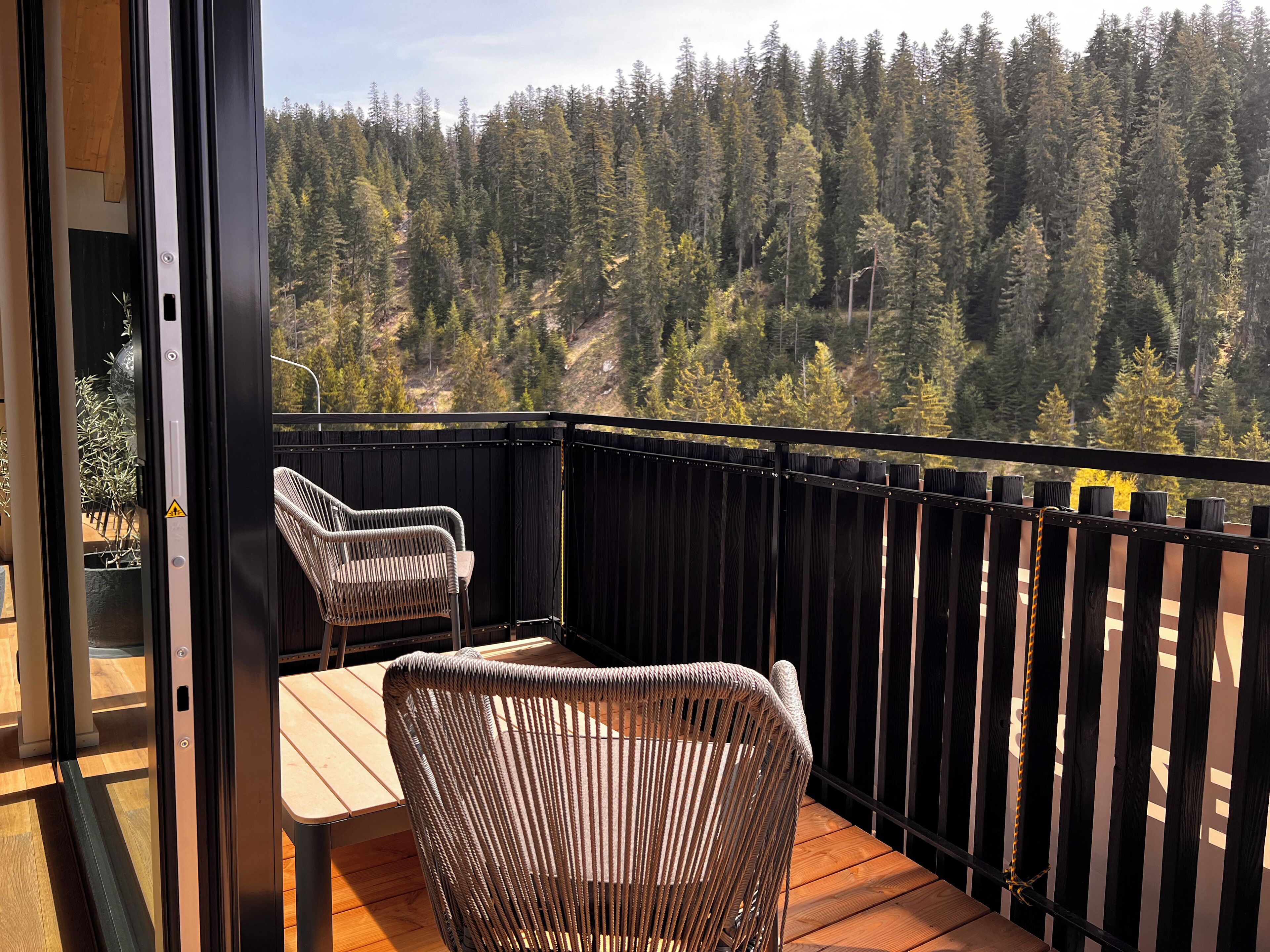 Un balcon avec deux fauteuils en osier et une table, donnant sur une colline boisée.