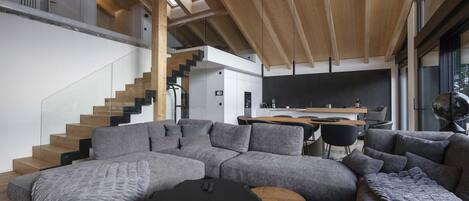 Una sala de estar moderna con un sofá seccional, una mesa redonda de centro y una escalera que conduce a un nivel superior.