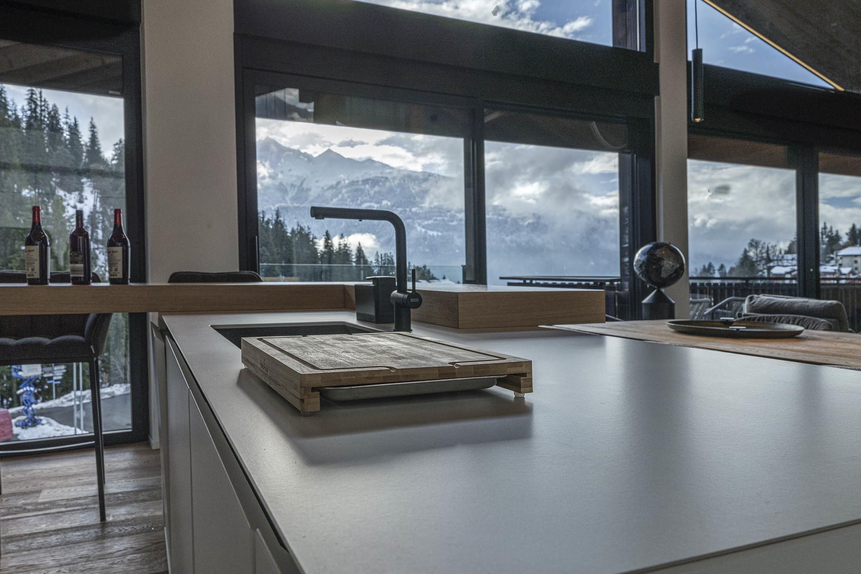 A modern kitchen with a large window overlooking a snowy mountain landscape.