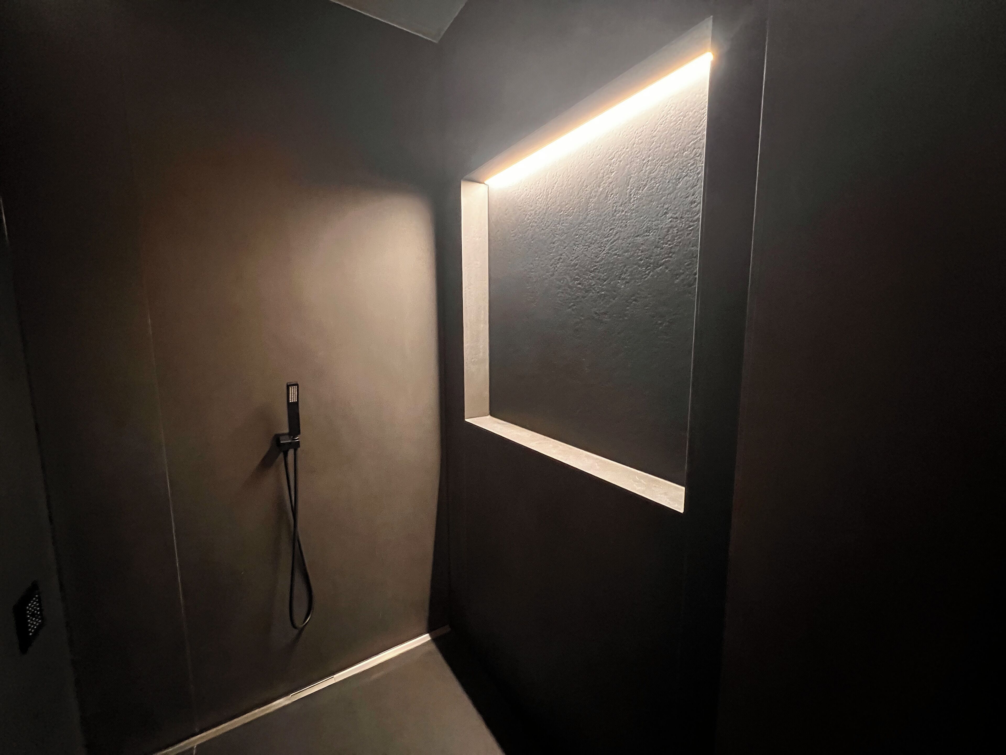 Une salle de bain moderne avec un mur de couleur sombre, une douche intégrée et une petite fenêtre agrémentée d’un bandeau lumineux.
