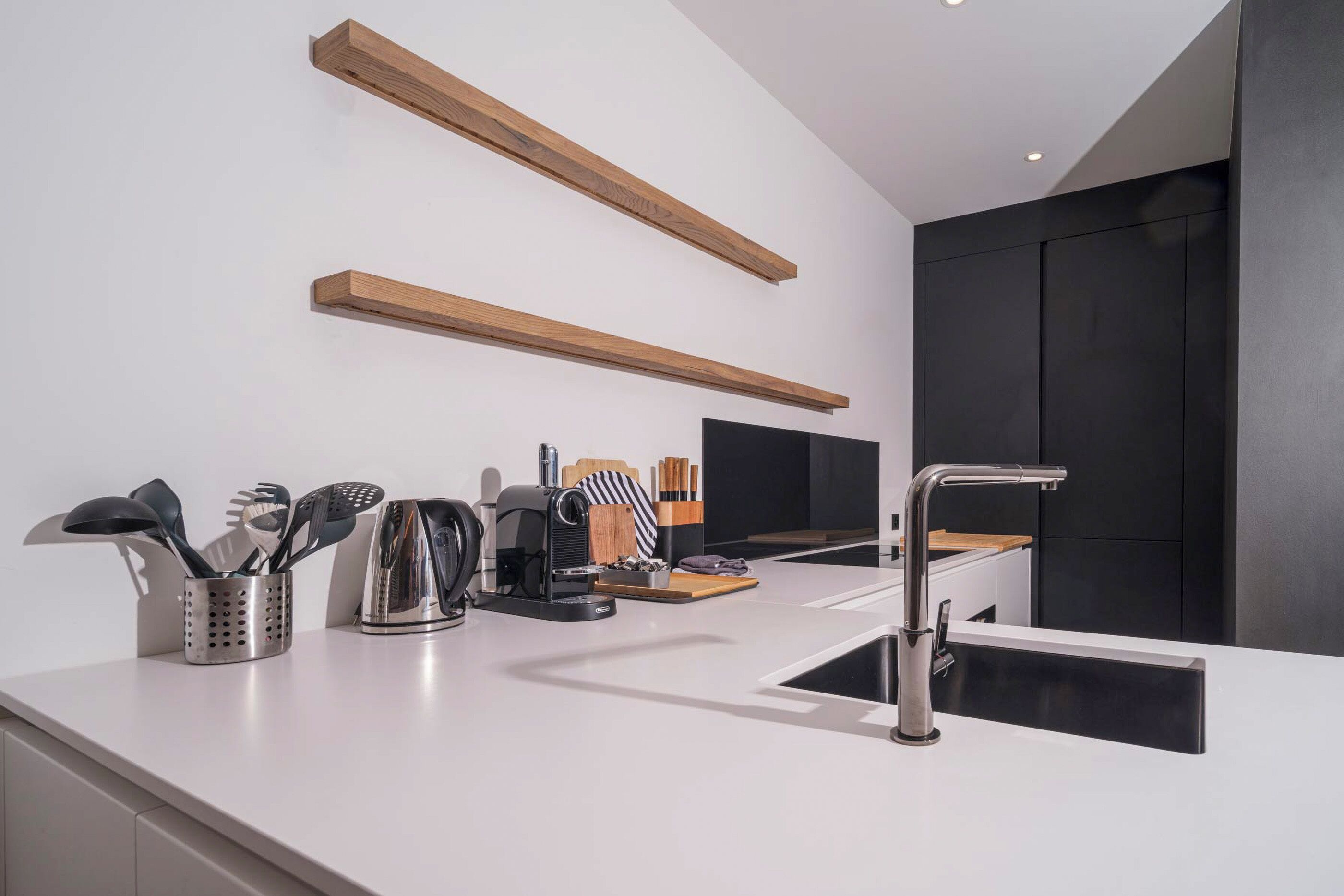 A modern kitchen with white countertops, a stainless steel sink, wooden shelves, and kitchen appliances.