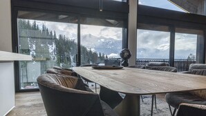 Un comedor moderno con una amplia mesa de madera y sillas cómodas, grandes ventanales que ofrecen vistas a montañas nevadas.