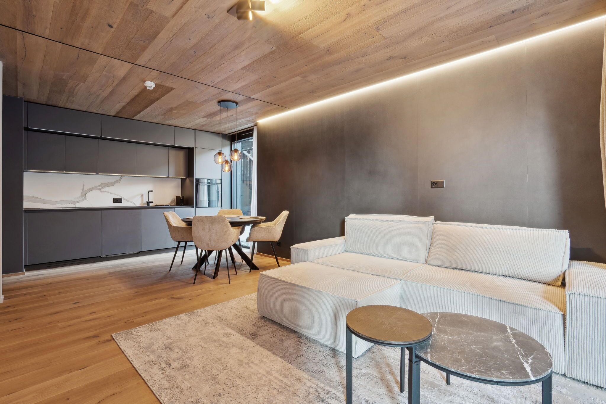 Ein zeitgemäßer Wohnraum mit Holzboden, einer Couch, einem runden Tisch und einer Küchenzeile mit Esstisch.