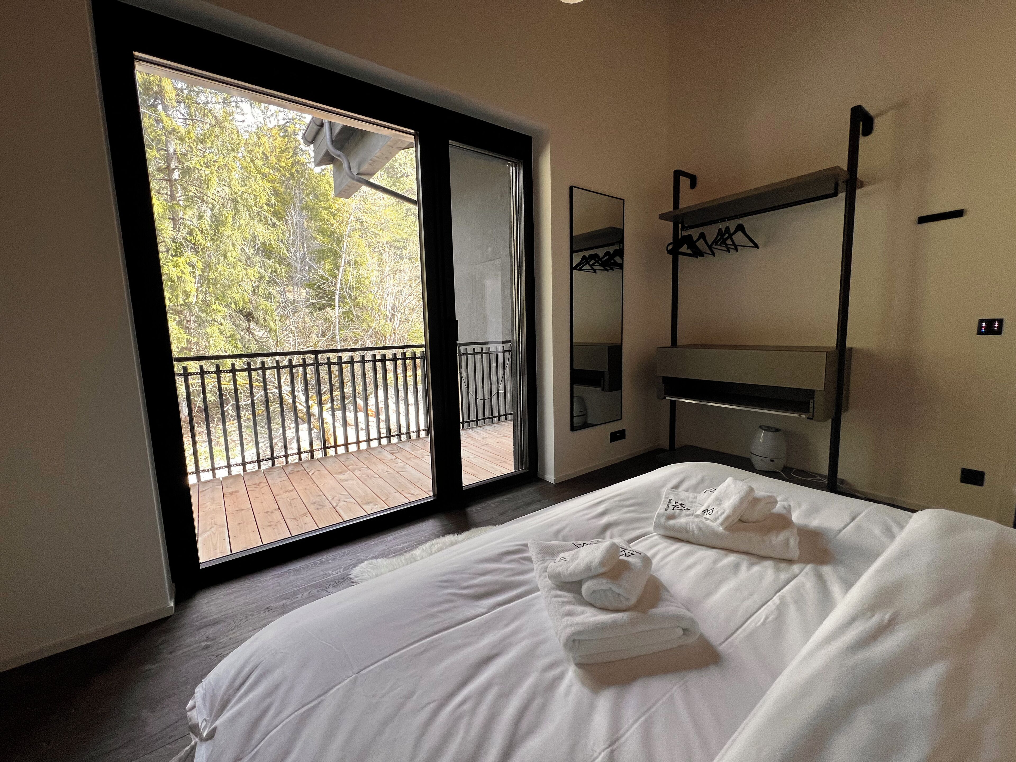 Hotelkamer met een groot bed, een balkon met uitzicht op bomen, een spiegel en een plank met handdoeken.