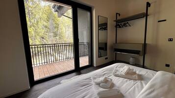 Hotelkamer met een groot bed, een balkon met uitzicht op bomen, een spiegel en een plank met handdoeken.
