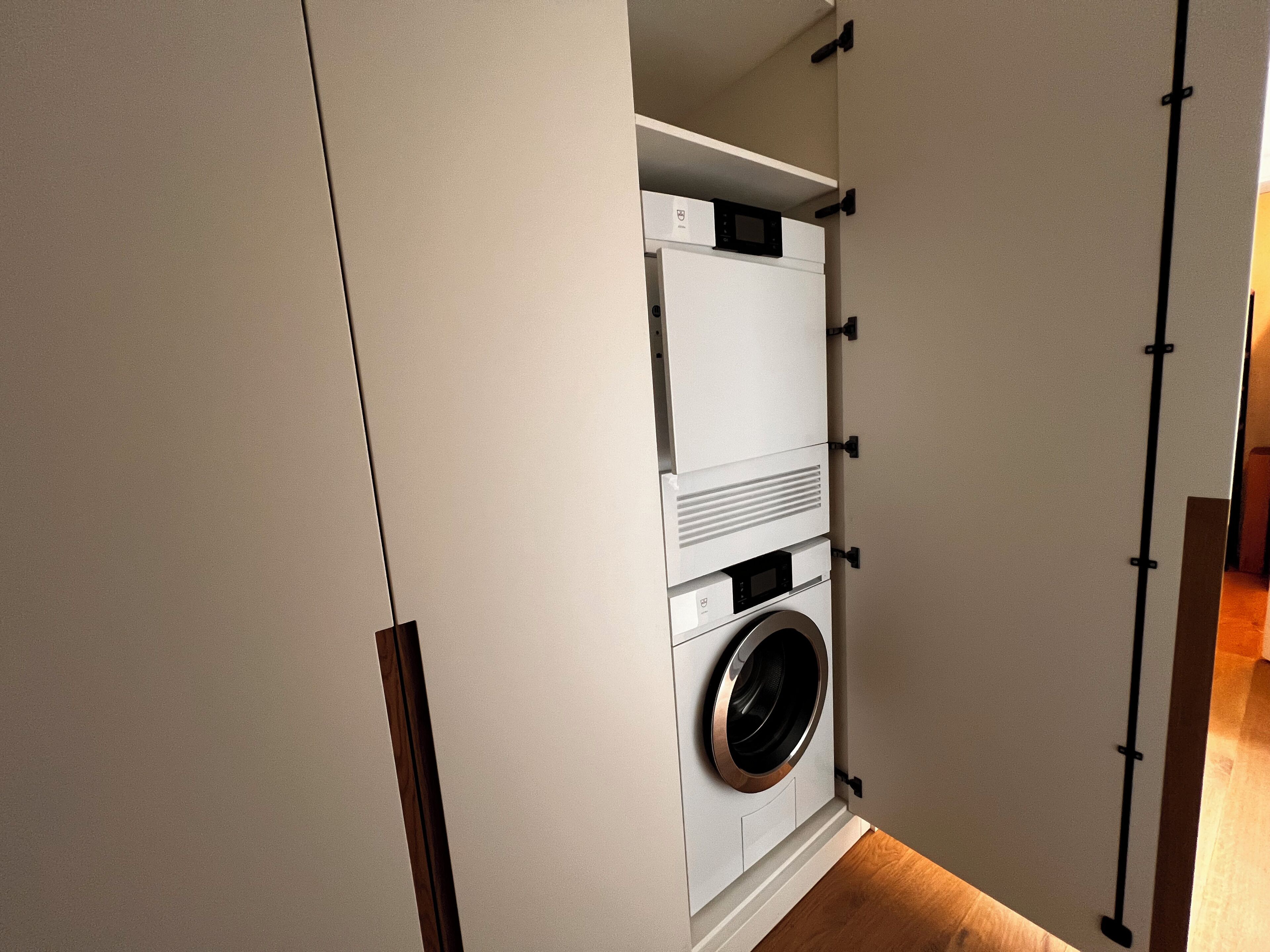 Ein kleiner Waschraum mit integrierter Waschmaschine und Trockner, umgeben von einem weißen Schrank mit schwarzen Griffen.