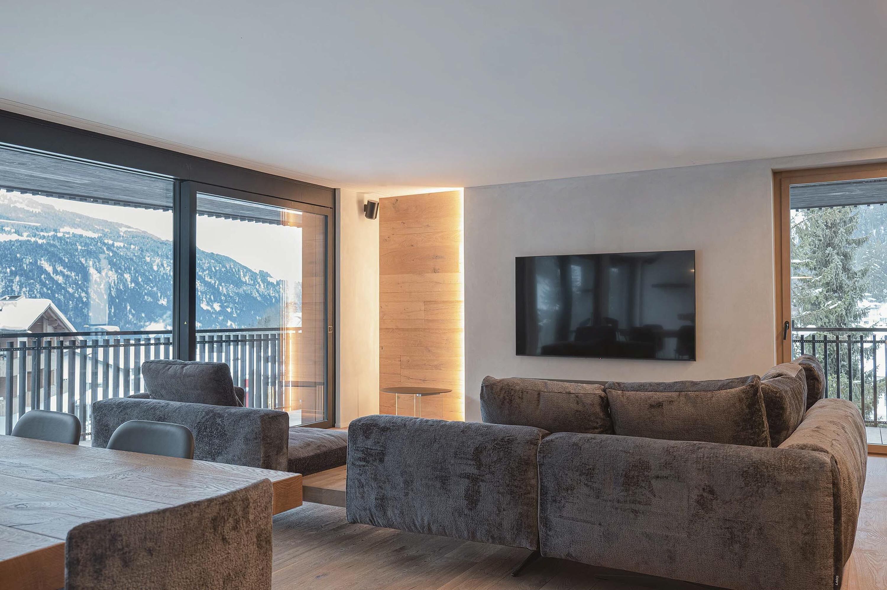 Un soggiorno moderno con una grande TV, posti a sedere comodi e un balcone con vista sulle montagne.