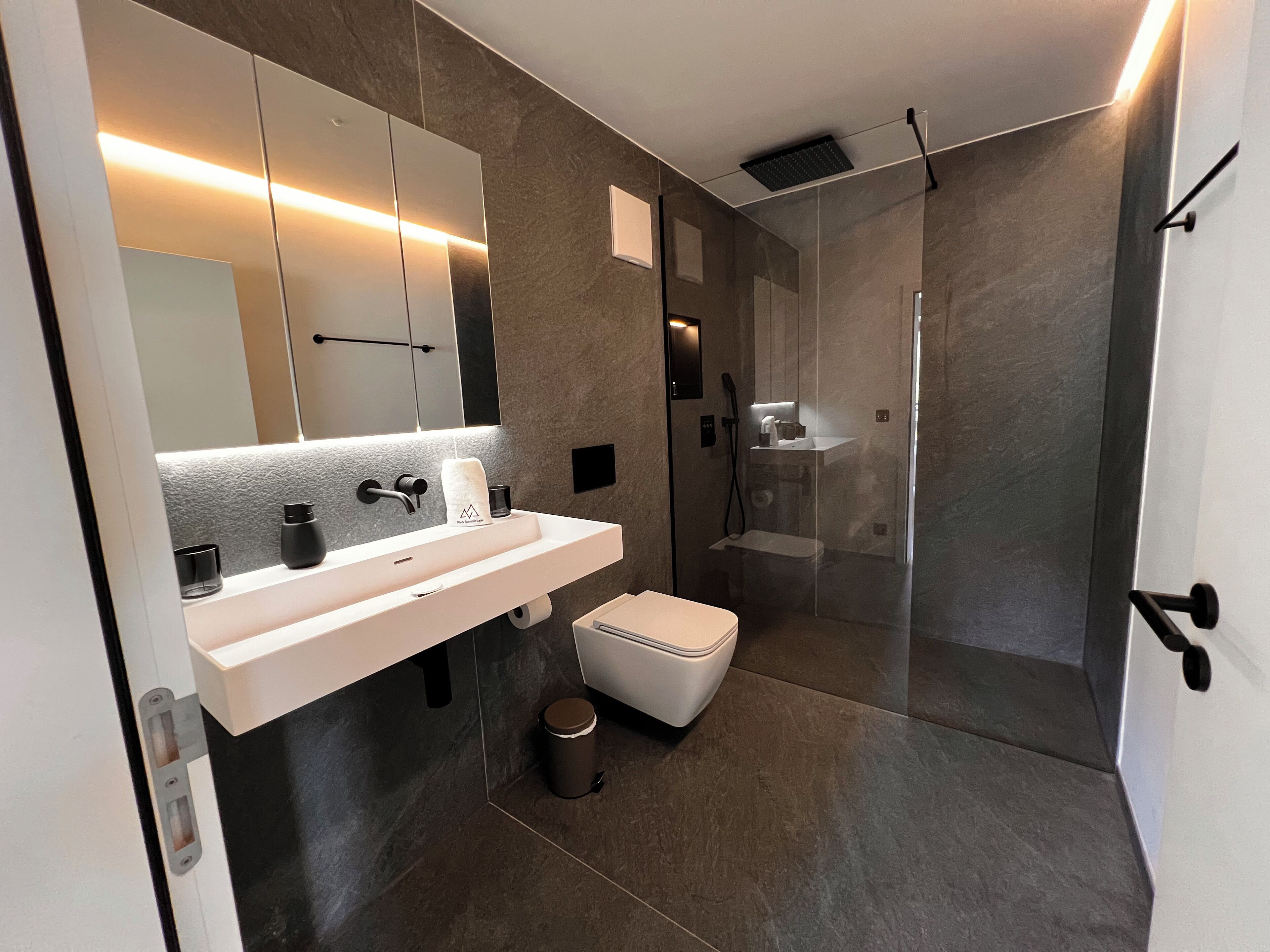 A modern bathroom with a large mirror, two sinks, a toilet, and a shower area.