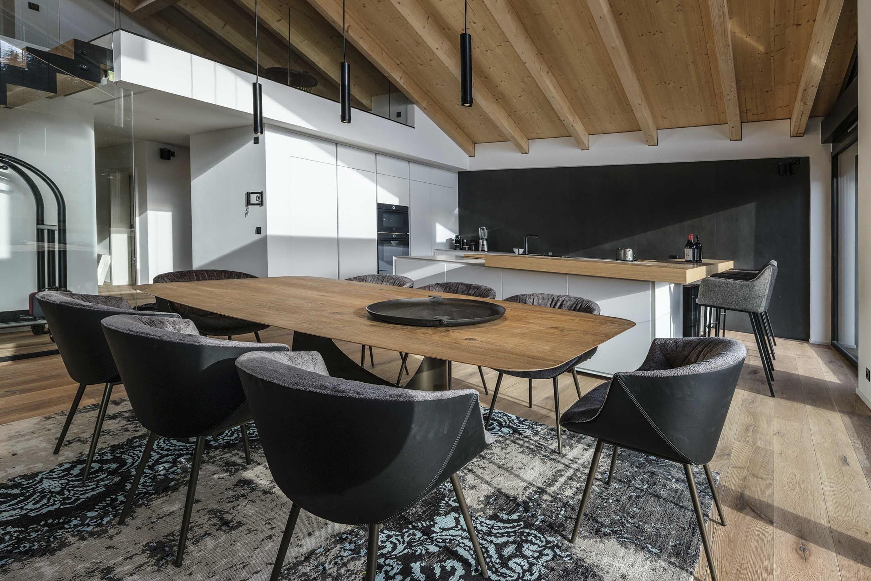 Une cuisine moderne avec un îlot en bois, des chaises noires et une grande table à manger.