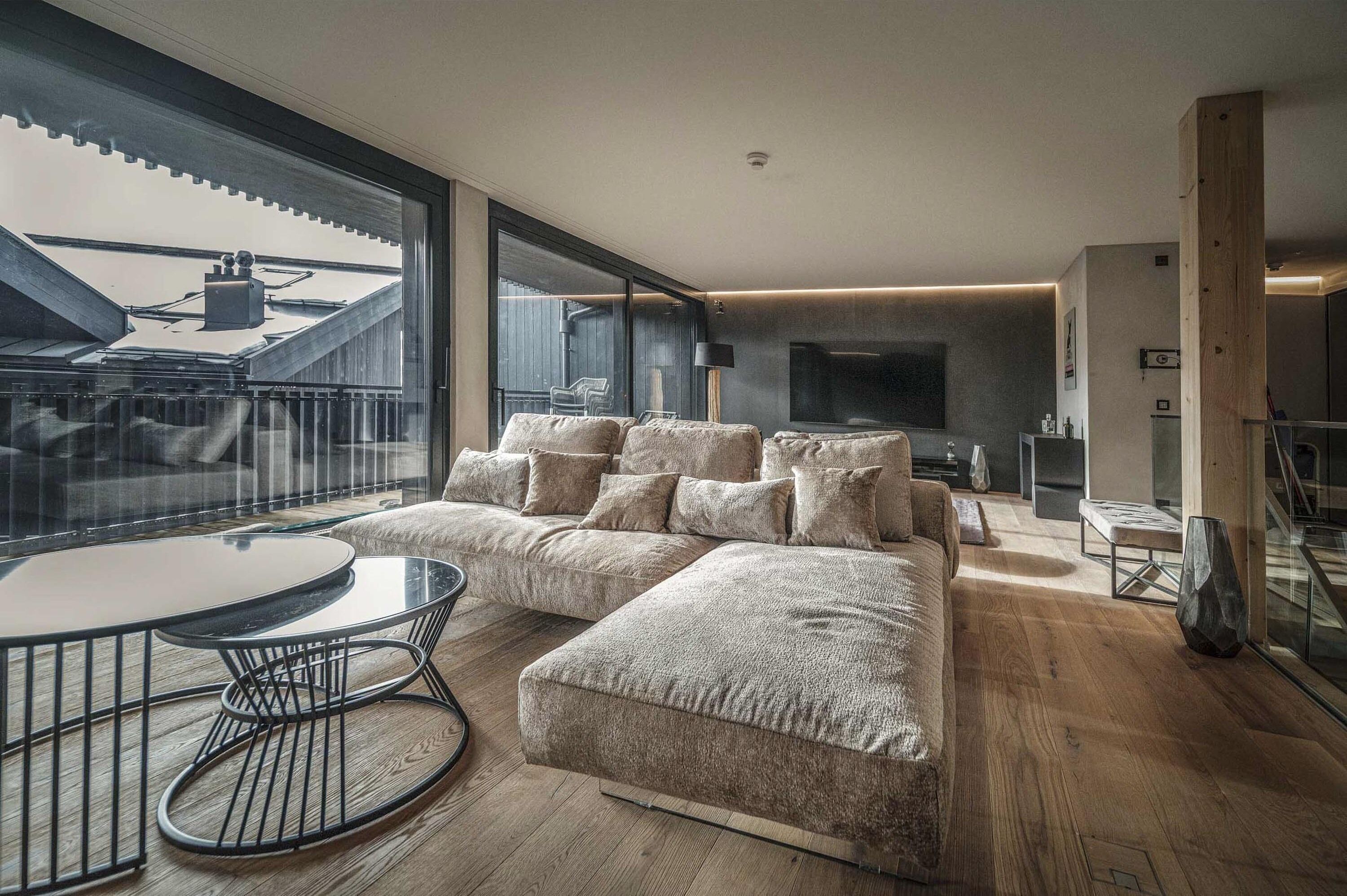 Una sala de estar moderna con un sofá seccional, una mesa redonda de vidrio y un ventanal con vistas a un edificio.