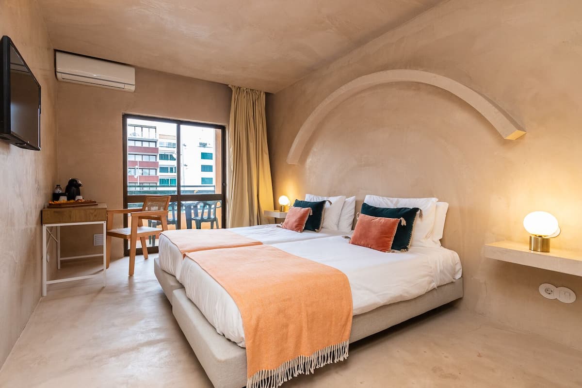 Une chambre d’hôtel avec un grand lit, un bureau avec une chaise, une fenêtre donnant sur des immeubles et un téléviseur fixé au mur.