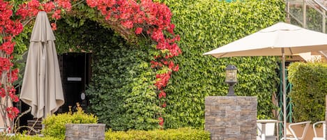 A restaurant with a green leafy wall, outdoor seating, and a stone wall.