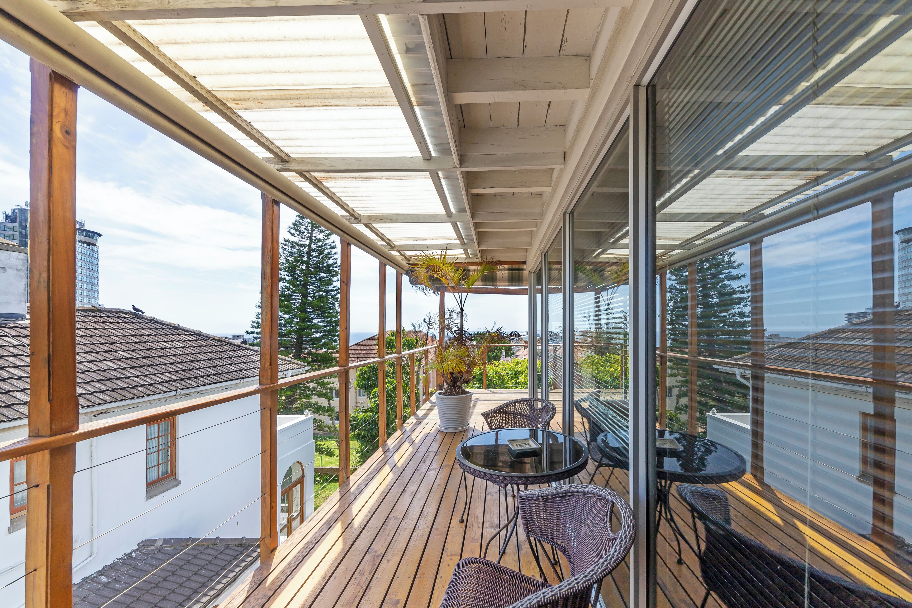 A covered balcony with wooden flooring, a glass railing, and a table with chairs.