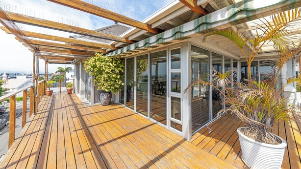 Un terrazzo in legno con piante in vaso, porte vetrate e vista sulla città.