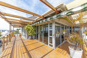 A wooden deck with potted plants, glass doors, and a view of the city. - Anchor Bay Workation (Cape Town)