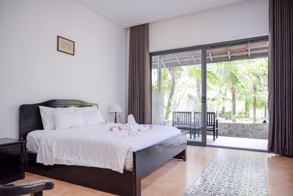 A hotel room with a bed, a nightstand, a chair, a table, and a view of palm trees through a glass door.