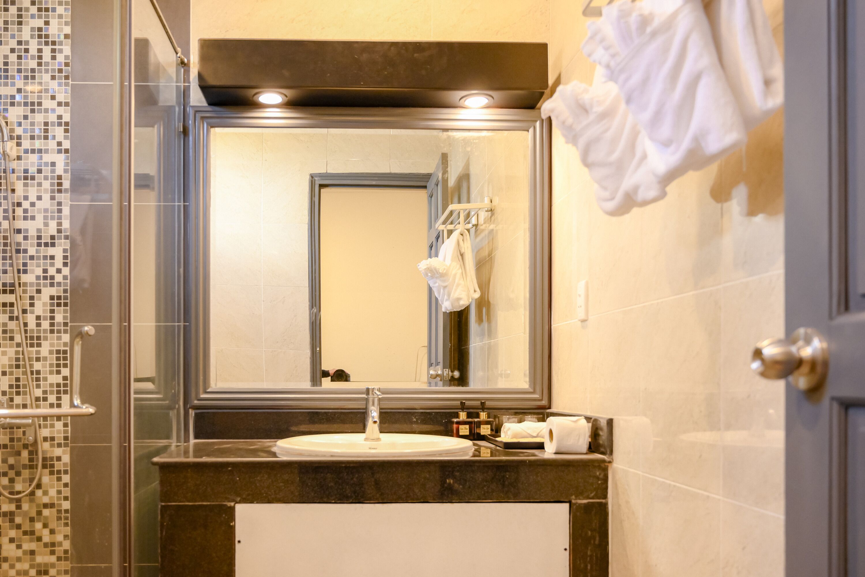 Un baño con ducha acristalada, un lavamanos con espejo y un perchero con toallas.