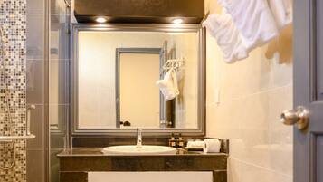 Un baño con ducha acristalada, un lavamanos con espejo y un perchero con toallas.