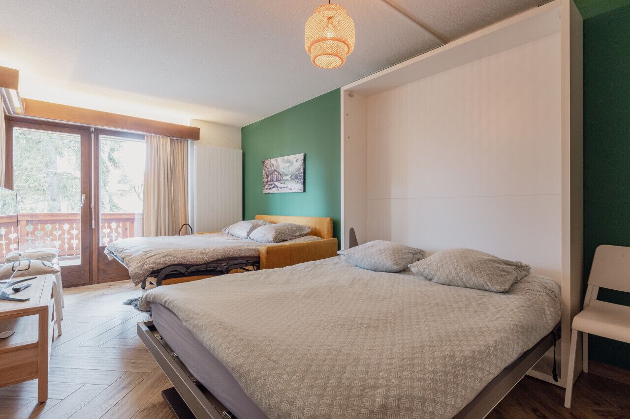 A bedroom with two beds, a wooden desk, and a balcony with curtains.
