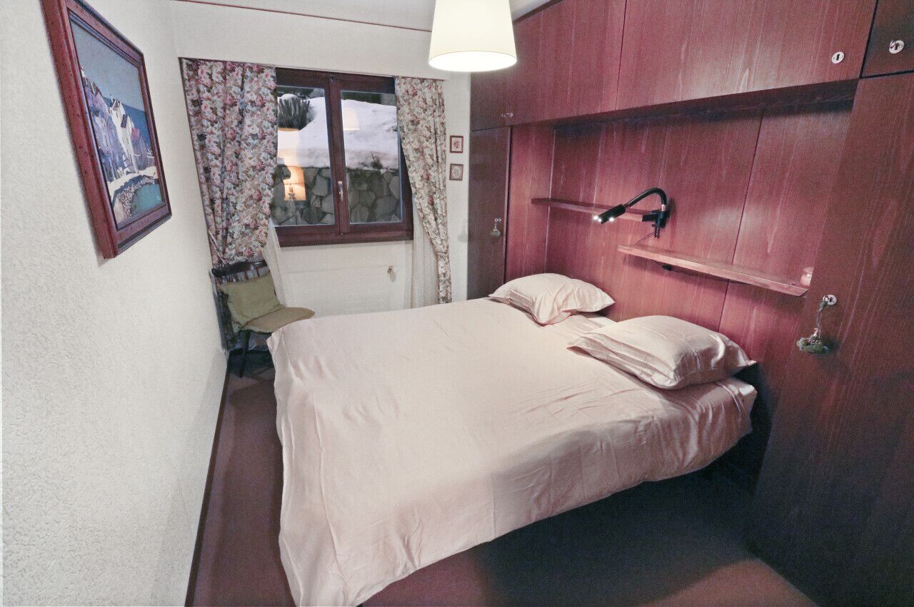 Una camera da letto con un letto, una finestra con tende, una lampada da comodino e un armadio in legno.