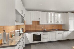 A modern kitchen with white cabinets, a black countertop, and a tiled backsplash. - Logement Spacieux au Coeur du Val D'illiez (Val-d'Illiez)