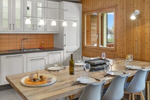 A modern kitchen with white cabinets, a wooden countertop, and a dining area with a table set for four. - Logement Spacieux au Coeur du Val D'illiez (Val-d'Illiez)