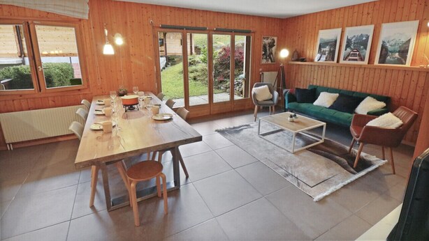 A cozy living room with a wooden interior, a dining area with a table set for four, and a green sofa.