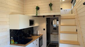 A compact kitchen with white cabinetry, a black countertop, and a microwave. There is a small sink and a wooden staircase to the right.