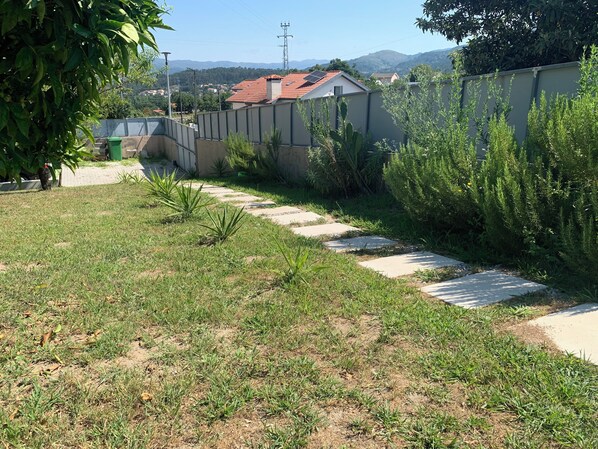 Un chemin de jardin bordé de gazon et de plantes, qui mène à une maison avec un toit rouge.