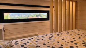 A bedroom with a bed, a window with a view, wooden walls, and a ceiling with recessed lighting.