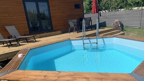 A rectangular pool with a wooden deck surrounding it, a ladder, and a table with chairs.