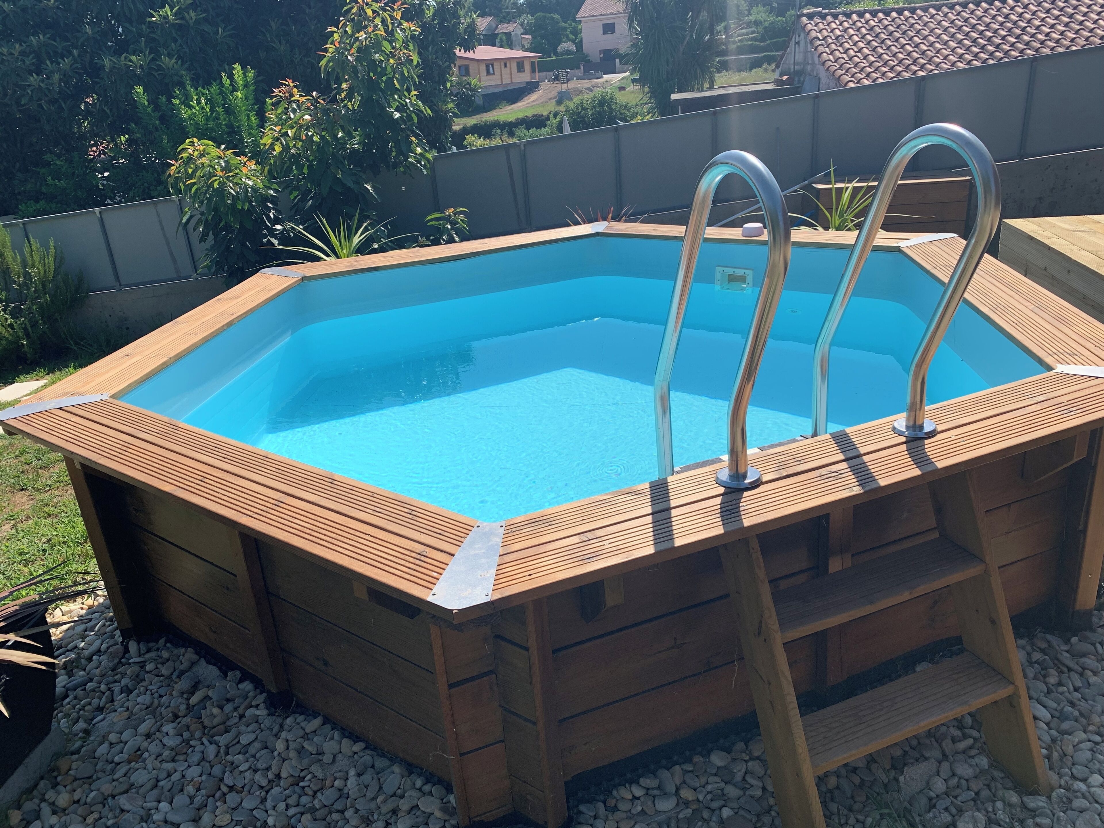 A wooden hot tub with metal ladders, surrounded by pebbles and a wooden deck.