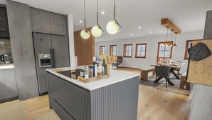 Una cocina moderna con una isla central, electrodomésticos integrados e iluminación colgante.