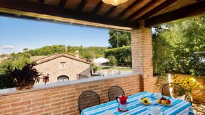 Une terrasse avec une table dressée pour le petit-déjeuner, offrant une vue sur un paysage rural avec des bâtiments en pierre et une végétation luxuriante.