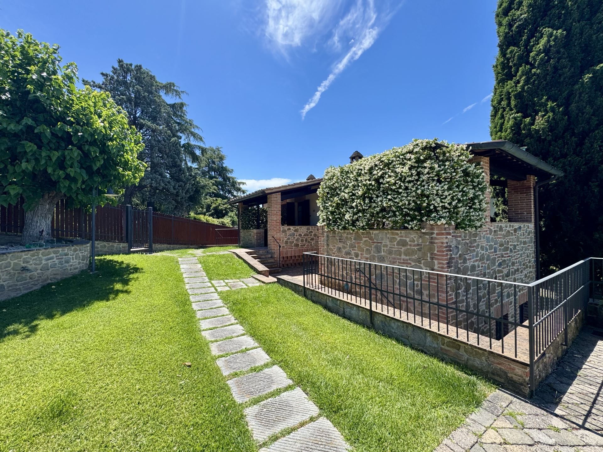 A well-maintained outdoor area with a stone pathway leading to a building with a brick facade and a white flowering hedge.