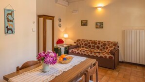 Uma sala de estar aconchegante com uma mesa de jantar de madeira, sofá floral e um vaso de flores.
