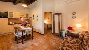 Cozinha aconchegante com armários de madeira, uma mesa de jantar com cadeiras, uma televisão e uma cama no quarto vizinho.