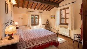 A bedroom with a bed, a nightstand, a lamp, a window with curtains, a radiator, and a wooden ceiling. - Agriturismo Case Graziani - Frantoio 3 (Citta della Pieve)